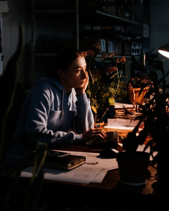Empreendedora pensativa diante do computador, à noite, num escritório escuro